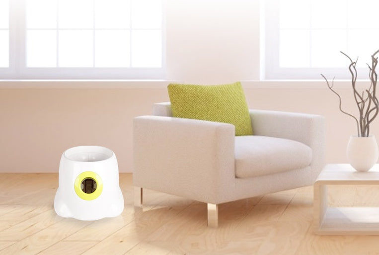 The white launcher with a yellow-rimmed side port standing on a wooden floor beside a cream armchair in a bright living room