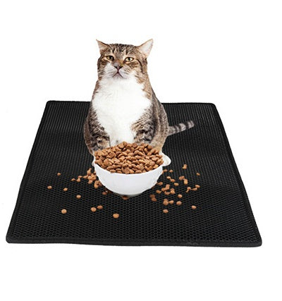 Black honeycomb litter mat with a tabby cat sitting behind a white bowl of dry food and kibble scattered across the surface