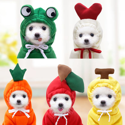 Five-panel collage of small white dogs indoors wearing frog, red-heart, carrot, apple and banana hoodies, each tied with a bow at the neck