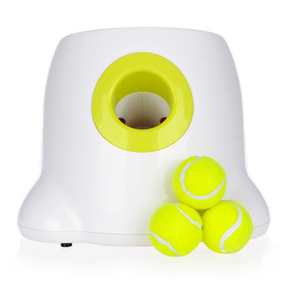 Head-on view of the white launcher on a white background, with a deep yellow-rimmed launch port in the front and three yellow tennis balls stacked beside it
