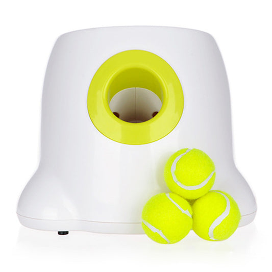 Head-on view of the white launcher on a white background, with a deep yellow-rimmed launch port in the front and three yellow tennis balls stacked beside it