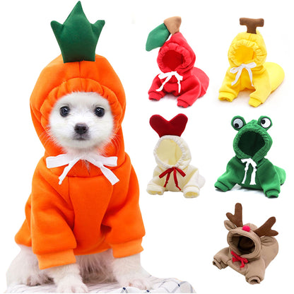 Small white dog wearing an orange carrot hoodie with a green leafy top, beside five unworn hoodies: apple, banana, cream with a red heart, frog and tan with antlers